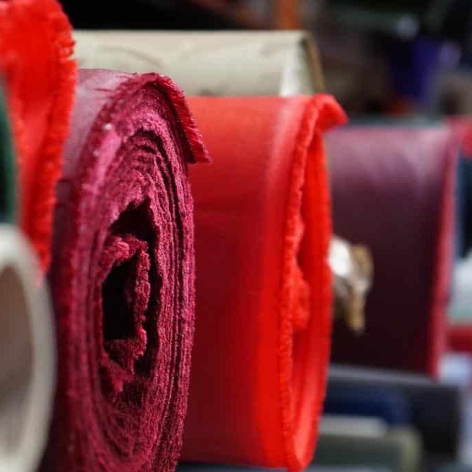 Rolls of different coloured textile material on a warehouse shelf.